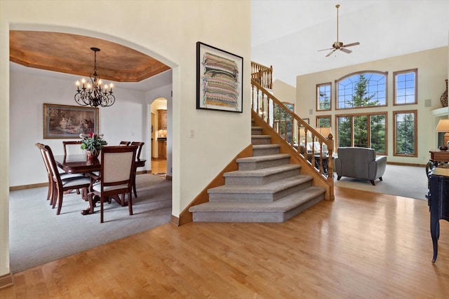 staircase with arched walkways, wood finished floors, a towering ceiling, baseboards, and a raised ceiling