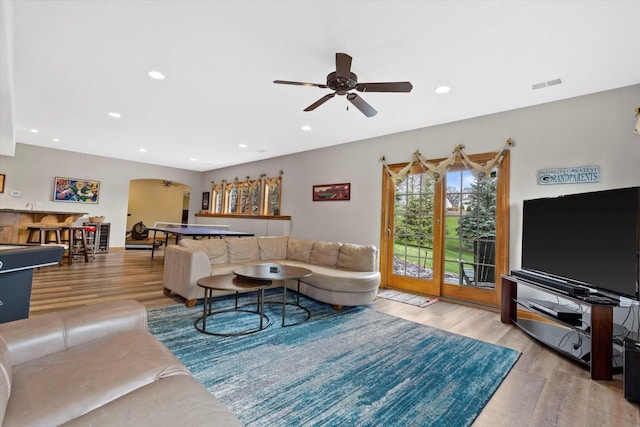 living room with a ceiling fan, visible vents, arched walkways, and wood finished floors