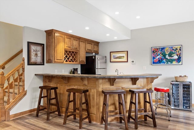 kitchen with wine cooler, a breakfast bar, wood finished floors, freestanding refrigerator, and a peninsula