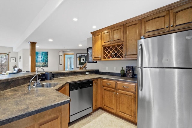 kitchen with appliances with stainless steel finishes, dark countertops, brown cabinetry, and a sink