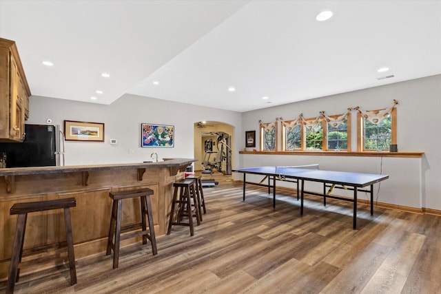 game room featuring arched walkways, recessed lighting, wood finished floors, baseboards, and wet bar