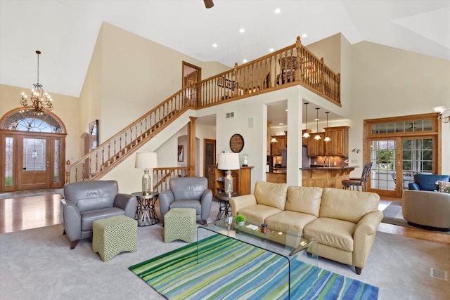 carpeted living room with high vaulted ceiling, visible vents, stairs, and a chandelier