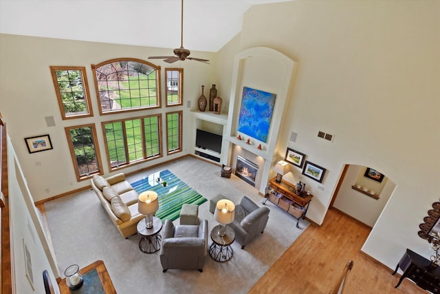 living room featuring visible vents, baseboards, a glass covered fireplace, ceiling fan, and high vaulted ceiling