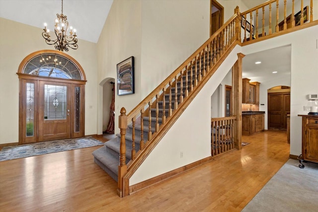 foyer with baseboards, arched walkways, wood finished floors, an inviting chandelier, and high vaulted ceiling