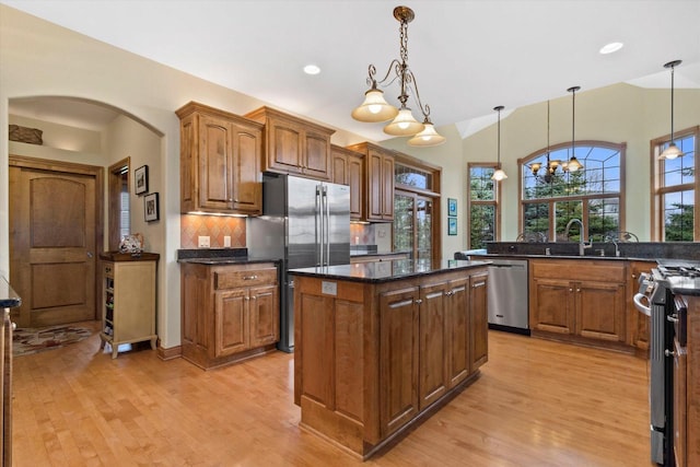 kitchen with stainless steel appliances, backsplash, a kitchen island, a sink, and light wood-type flooring