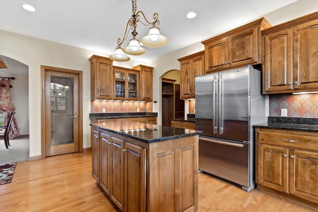 kitchen featuring a center island, arched walkways, glass insert cabinets, freestanding refrigerator, and brown cabinetry