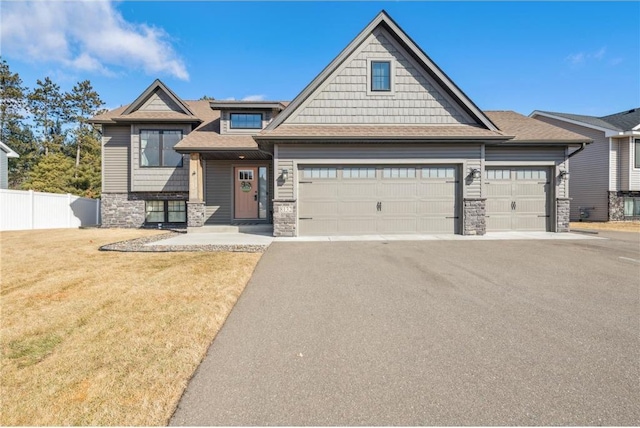 view of front facade featuring stone siding, fence, aphalt driveway, and a front yard