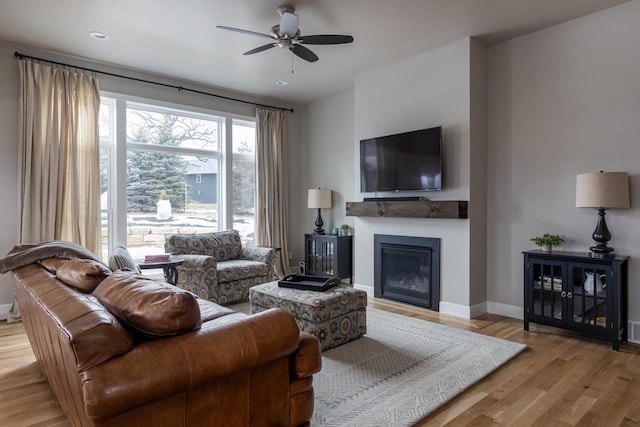 living room featuring a ceiling fan, baseboards, wood finished floors, and a glass covered fireplace