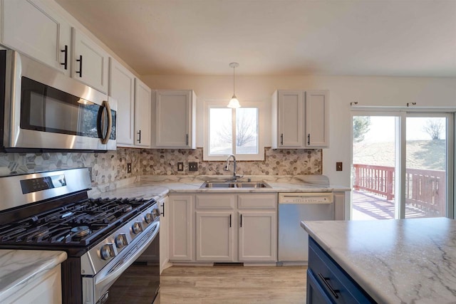 kitchen featuring light wood finished floors, hanging light fixtures, backsplash, appliances with stainless steel finishes, and a sink