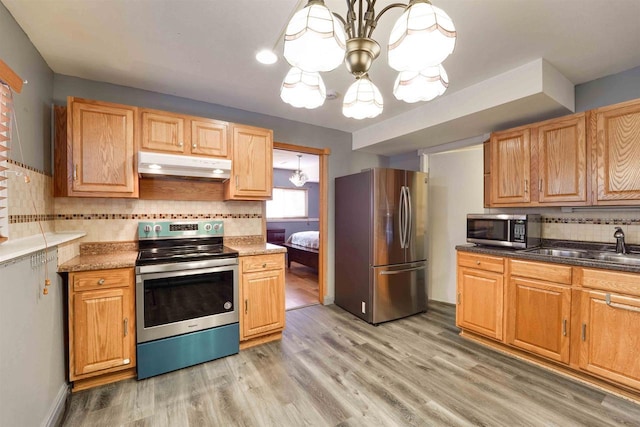 kitchen featuring appliances with stainless steel finishes, light wood-type flooring, an inviting chandelier, and under cabinet range hood