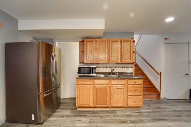 kitchen featuring light wood-style flooring, a sink, appliances with stainless steel finishes, decorative backsplash, and dark countertops