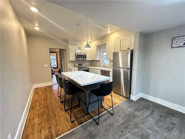 kitchen with baseboards, white cabinets, a kitchen island, a kitchen breakfast bar, and stainless steel appliances