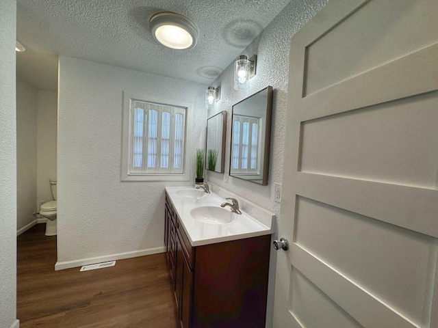 full bathroom with a textured wall, a sink, toilet, and wood finished floors