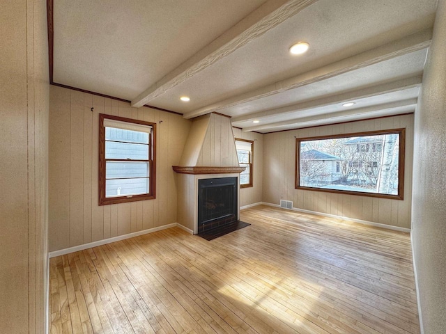 unfurnished living room with light wood finished floors, beamed ceiling, visible vents, and a healthy amount of sunlight