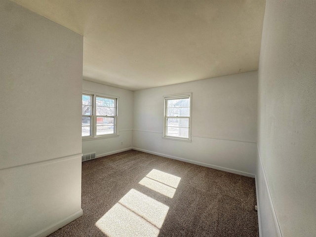 spare room featuring plenty of natural light, carpet flooring, visible vents, and baseboards