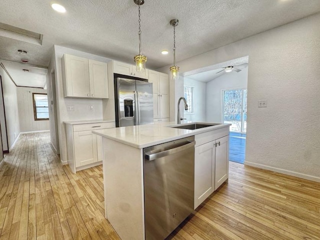 kitchen featuring light countertops, a textured wall, appliances with stainless steel finishes, a sink, and light wood-type flooring