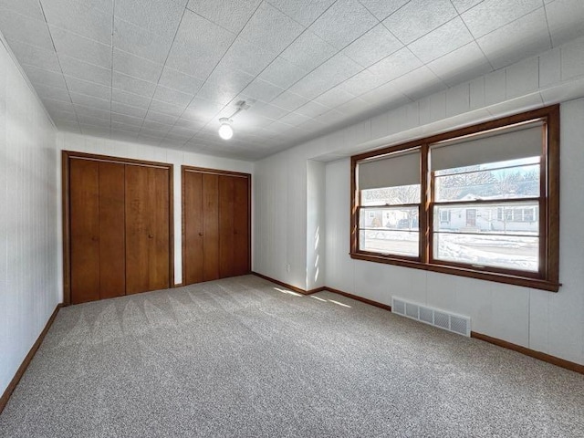 unfurnished bedroom featuring multiple windows, visible vents, two closets, and carpet flooring