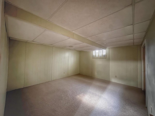 basement featuring a paneled ceiling and wooden walls