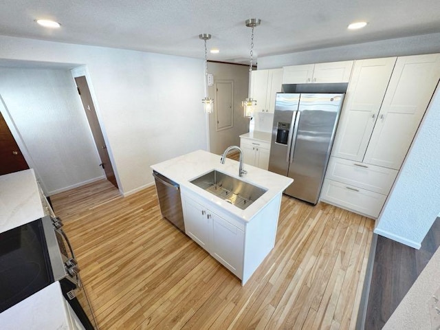 kitchen featuring appliances with stainless steel finishes, hanging light fixtures, light wood-style floors, white cabinetry, and a sink