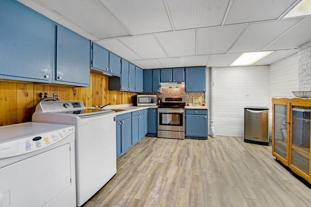 laundry room with washing machine and dryer, a sink, wooden walls, light wood-type flooring, and laundry area