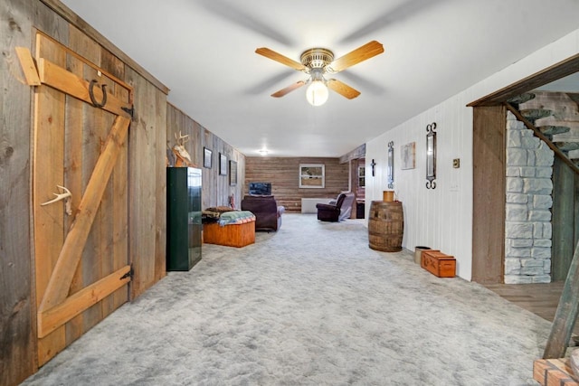 living area featuring wood walls, a ceiling fan, and carpet flooring