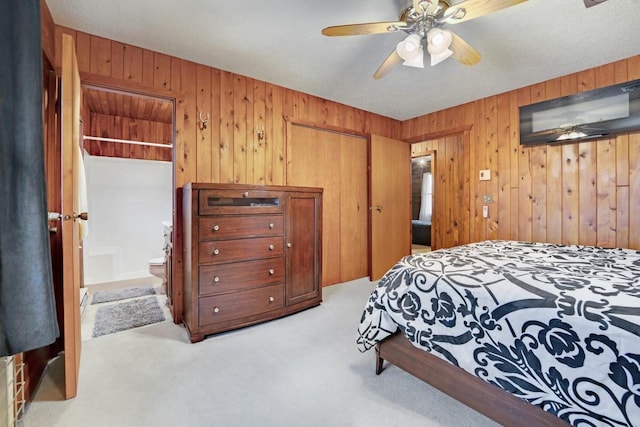 carpeted bedroom featuring a ceiling fan, a closet, wooden walls, and ensuite bathroom