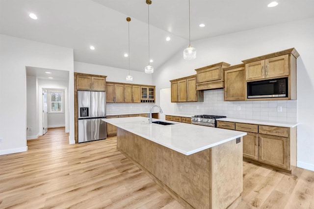 kitchen with a kitchen island with sink, stainless steel appliances, a sink, light wood finished floors, and brown cabinetry