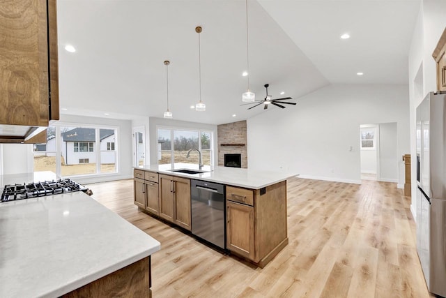 kitchen featuring stainless steel appliances, a fireplace, a sink, light countertops, and light wood-type flooring