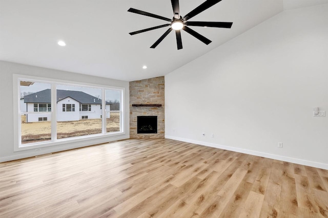 unfurnished living room featuring light wood-style floors, vaulted ceiling, a stone fireplace, and baseboards