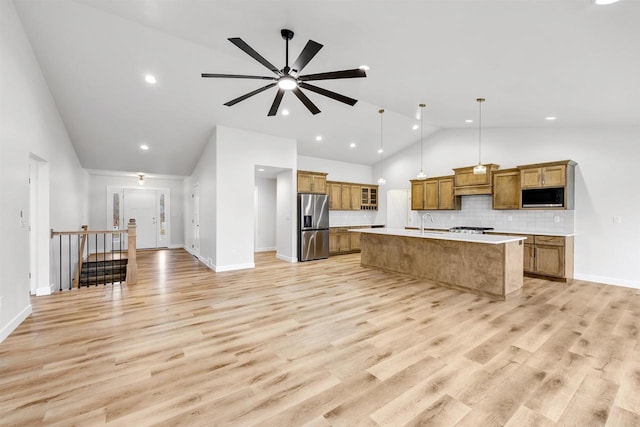 kitchen with stainless steel refrigerator with ice dispenser, light countertops, brown cabinetry, a kitchen island with sink, and black microwave