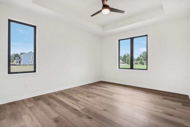 empty room with a raised ceiling, baseboards, and wood finished floors