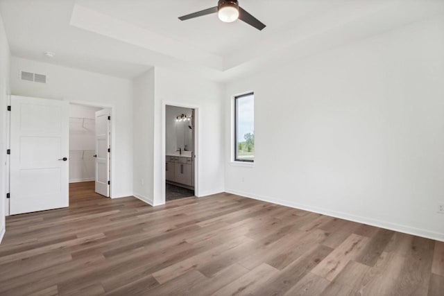 unfurnished bedroom with a tray ceiling, wood finished floors, visible vents, and baseboards