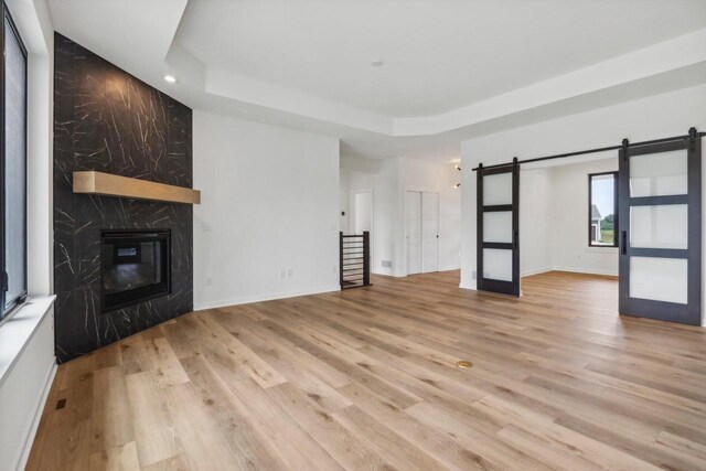 unfurnished living room with a fireplace, light wood finished floors, a raised ceiling, a barn door, and baseboards