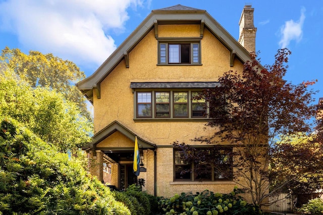 view of front of house with brick siding, stucco siding, and a chimney