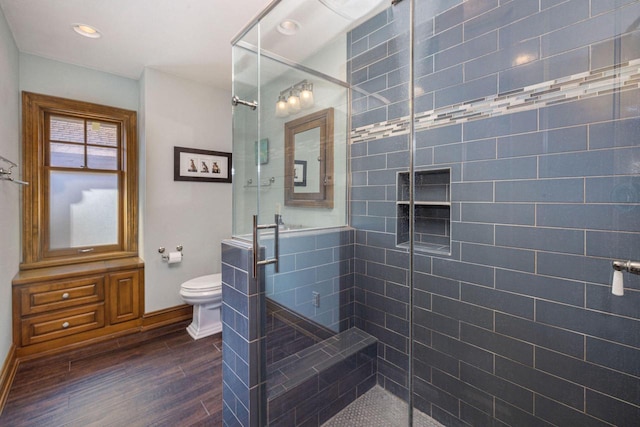 bathroom with a shower stall, toilet, baseboards, and wood finished floors