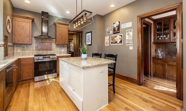 kitchen featuring wall chimney range hood, a breakfast bar area, light wood finished floors, and stainless steel appliances