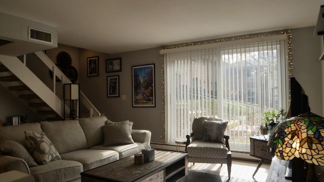 living room with a baseboard heating unit, stairs, visible vents, and wood finished floors