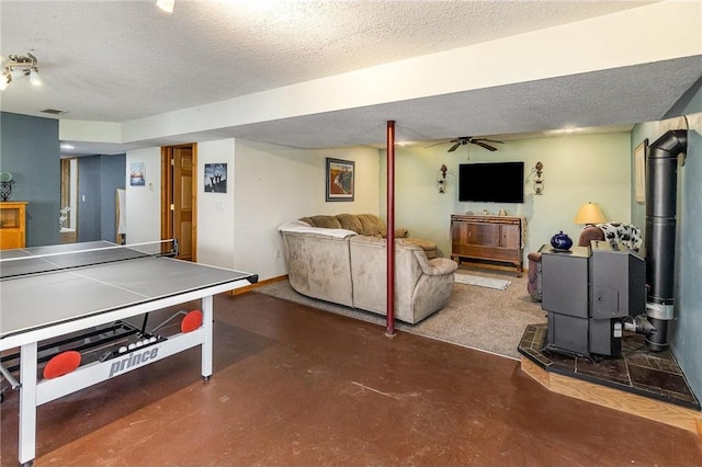 rec room featuring finished concrete floors, a wood stove, a ceiling fan, and a textured ceiling