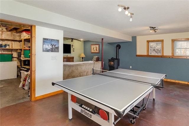 recreation room featuring concrete floors, a wood stove, and baseboards