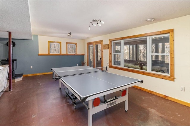 rec room featuring a textured ceiling, a wood stove, and baseboards