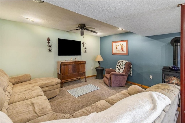 living area featuring baseboards, carpet floors, a wood stove, a textured ceiling, and a ceiling fan