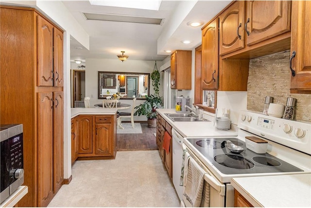 kitchen with brown cabinets, white appliances, light countertops, and a sink