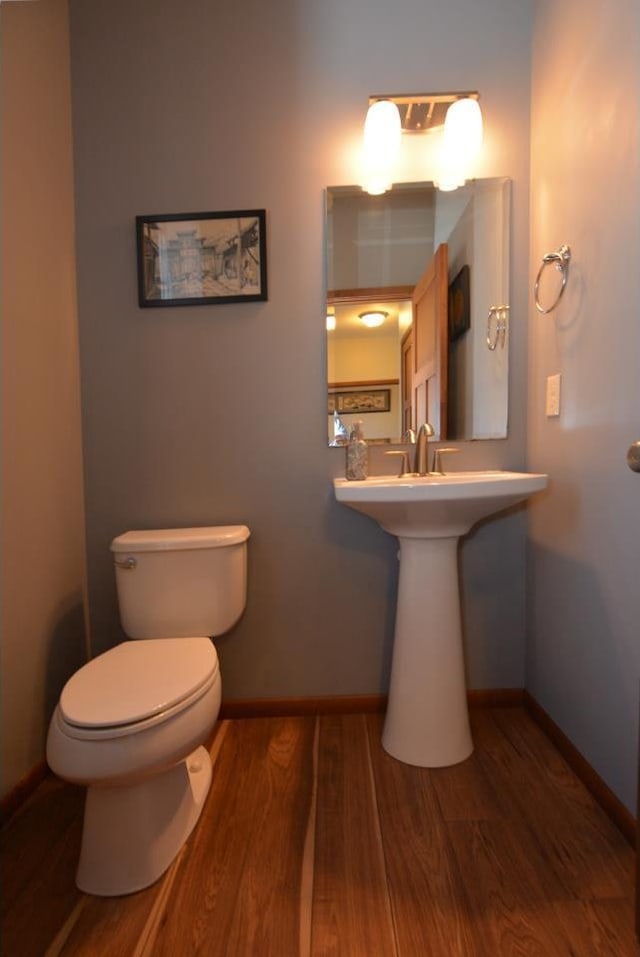 half bathroom featuring wood finished floors, toilet, and baseboards