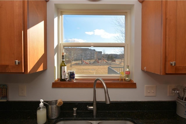 kitchen with brown cabinetry, dark countertops, and a sink