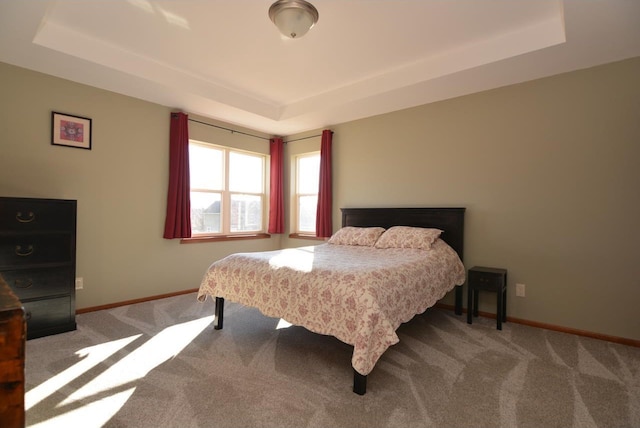 carpeted bedroom featuring a tray ceiling and baseboards