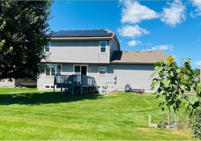 rear view of property with roof mounted solar panels, a lawn, a deck, and stairs