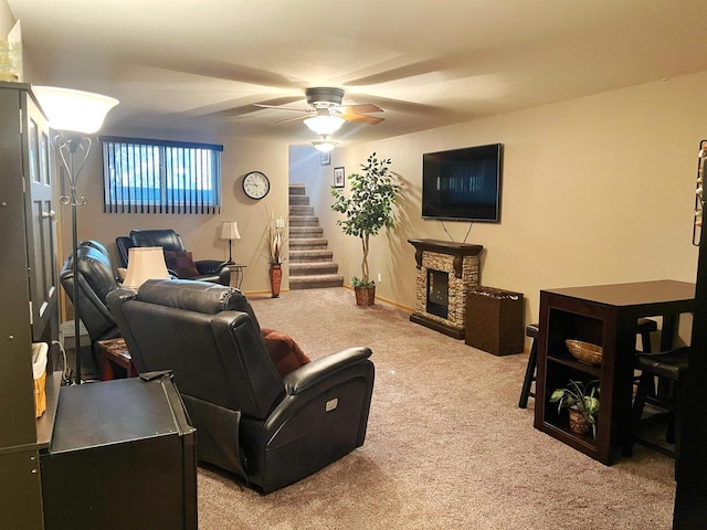 carpeted living room featuring ceiling fan, stairway, baseboards, and a stone fireplace