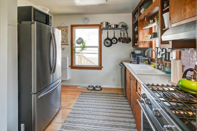 kitchen featuring light wood finished floors, a sink, light countertops, stainless steel appliances, and open shelves