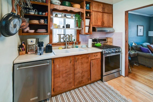 kitchen featuring light wood-type flooring, a sink, open shelves, appliances with stainless steel finishes, and wall chimney range hood