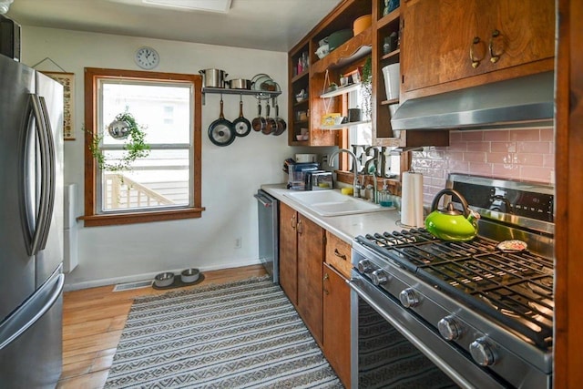 kitchen with under cabinet range hood, light countertops, decorative backsplash, light wood-style floors, and stainless steel appliances